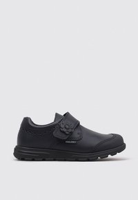 Zapato de cuero negro con punta redonda y correa de velcro. Presenta un acento decorativo de flor y detalles perforados en la parte superior. Suela de goma.