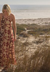 Maxi dress with a halter neckline, featuring bold geometric patterns in maroon and beige. The fabric appears lightweight and textured.