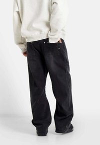 Zwarte relaxed-fit jeans met een recht model, voorzien van achterzakken en zilveren hardware accenten. Geregistreerd met een lichtgrijze sweatshirt.