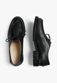 Zapatos de cuero negro con un acabado texturizado, punta redondeada, diseño de cordones y suela de goma gruesa con un patrón estriado.