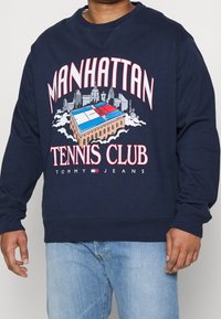 Felpa blu navy con una grafica di un campo da tennis e lo skyline della città. Il testo recita "MANHATTAN TENNIS CLUB" con accenti in rosso e bianco.