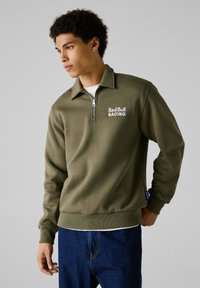 Sudadera verde oliva con cremallera de cuarto, con el logo "Red Bull RACING" en blanco, puños acanalados y dobladillo recto.