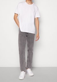 Camiseta blanca de algodón, jeans de mezclilla gris con costuras claras y zapatillas blancas. Ajuste casual, mangas cortas, pierna recta.