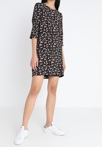 Mustat kukkakuosiset mini-mekko, jossa on kolme neljäsosaa hihat. Sisältää vaaleanpunaisia kukkakuviota kauttaaltaan. Yhdistetty valkoisiin tennareihin rentoa ilmettä varten.