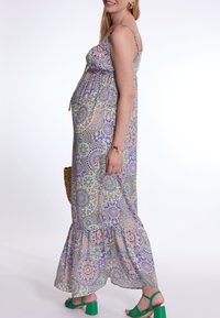 Multicolored maxi-jurk met bloemenpatronen, verstelbare bandjes en een rucheszoom. G gedragen met groene blokhak-sandalen en een geweven tas.