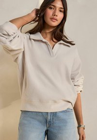 Pullover in pile beige chiaro con colletto e maniche oversize, abbinato a jeans in denim azzurro chiaro. Texture liscia e vestibilità casual.