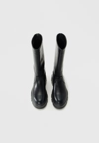 Paar hohe schwarze Lederstiefel mit dicken Sohlen, aufrecht auf einem weißen Hintergrund stehend, von oben betrachtet.