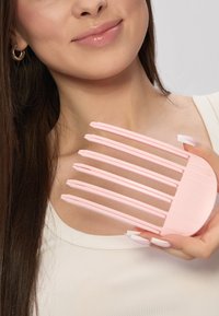 Rosa plastkam med fem brede tænder, der har en afrundet bund og teksten "GLOV" prægede. Håndholdt mod en lys baggrund.