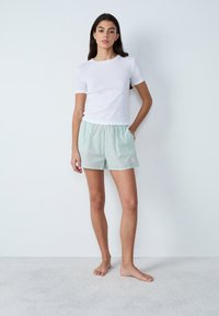 Camiseta blanca de manga corta combinada con pantalones cortos a cuadros verdes que cuentan con una cintura elástica y un pequeño detalle en forma de corazón rosa.