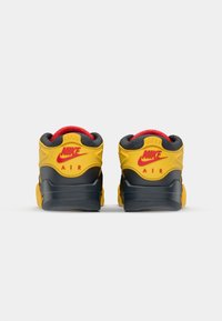 Nike Air-sneakers med en gul overdel, røde detaljer og en sort såle. Designet inkluderer polstrede kraver og teksturerte materialer.