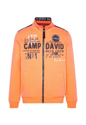 Sudadera naranja con cremallera y cuello alto, que presenta estampados y diseños en negro, y dos bolsillos frontales. Hecha de un tejido suave y texturizado.