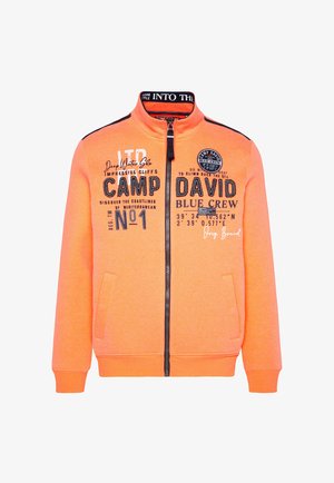 Sudadera naranja con cremallera y cuello alto, que presenta estampados y diseños en negro, y dos bolsillos frontales. Hecha de un tejido suave y texturizado.