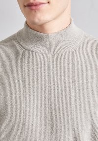 Pull à col roulé gris côtelé, avec un col haut et un tissu texturé. Vue en gros plan mettant en évidence le motif tricoté doux.