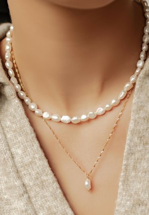 Due collane a strati: una presenta perle barocche bianche, l'altra una catena dorata attorcigliata con un semplice pendente a goccia di perla.