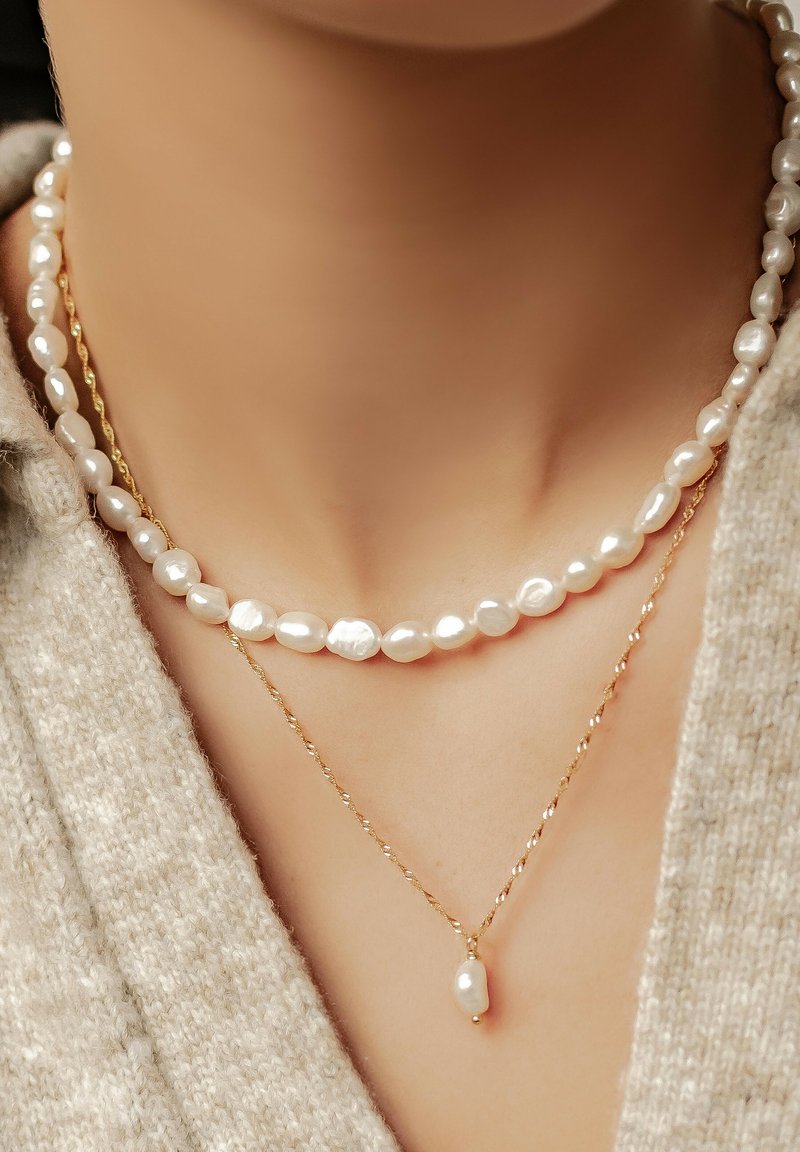 Dos collares en capas: uno presenta perlas barrocas blancas, y el otro una cadena dorada retorcida con un colgante de perla en forma de lágrima.