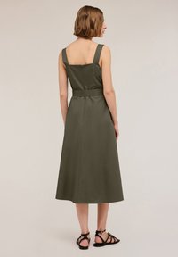 Kaki grön klänning med en figursydd bodice, breda axelband, en väldefinierad midja och en utsvängd maxikjol. Har en dragkedja bak.