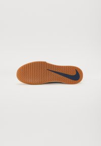 Nikeova potplat tenisice od gumenog materijala s uzorkom zupčastog profila; sadrži plavi swoosh logo sa strane; glatka tekstura.
