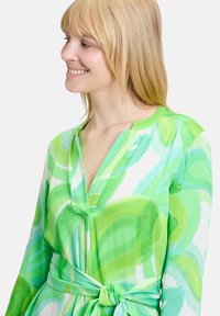 Grünes abstraktes Druckkleid aus leichtem Stoff, mit V-Ausschnitt, langen Ärmeln und einer gebundenen Taillendetail.