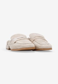 Mocasines de ante beige con puntera redondeada, con un detalle de costura y una suela de goma marrón claro baja. Diseño deslizante con una textura suave.