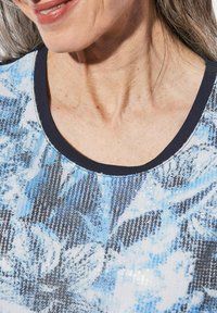 Blauw en wit gemusterde top met een ronde hals, voorzien van een textuur, paillettenontwerp en een effen marineblauwe rand langs de kraag.