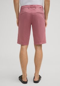 Pantaloni corti in cotone rosa con una vestibilità dritta, lunghezza al ginocchio, dotati di tasche posteriori e passanti per cintura, abbinati a sandali neri a scivolo.