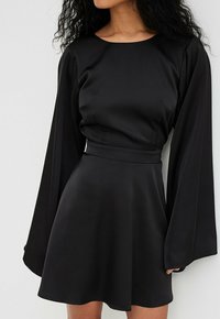 Robe en satin noir avec de longues manches fluides, un décolleté rond et une taille cintrée avec une jupe évasée. Texture lisse avec un design minimal.