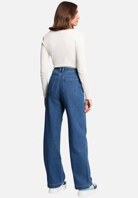Jean bleu taille haute, à jambe large, avec une texture denim classique et deux poches arrière, associés à un top ajusté à manches longues blanc.