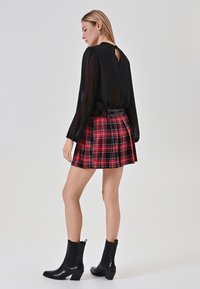 Schwarze, durchsichtige Bluse mit einem rückwärtigen Schlüssel-Loch. Roter, kariierter, plissierter Rock mit einem schwarzen Gürtel. Schwarze Stiefeletten mit leichtem Absatz.