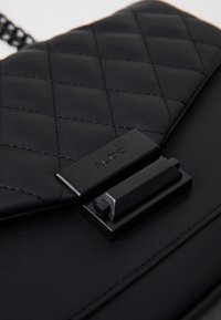 Borsa a tracolla nera in ecopelle trapuntata con elegante chiusura in metallo nero e hardware coordinato. Superficie testurizzata con dettagli di cucitura precisi.