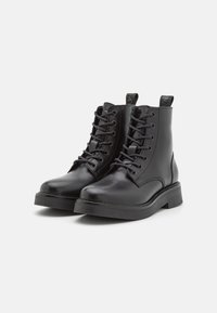 Botines de cuero negro hasta el tobillo con punteras redondas, diseño con cordones y suelas de goma planas. Presentan costuras en contraste y lengüetas en el talón.