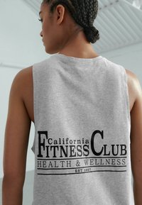 Šedé tílko bez rukávů s potiskem "California Fitness Club" tučným černým písmem, pod kterým je text "Health & Wellness" a údaj o založení 1997.