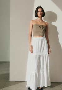 Olivi vihreä olkaimeton crop-top, jossa on solmittava etuosa, yhdistetty valkoiseen maksihameeseen, jossa on teksturoitu kangas ja kerroksellinen helma. Mustat sandaalit viimeistelevät asun.