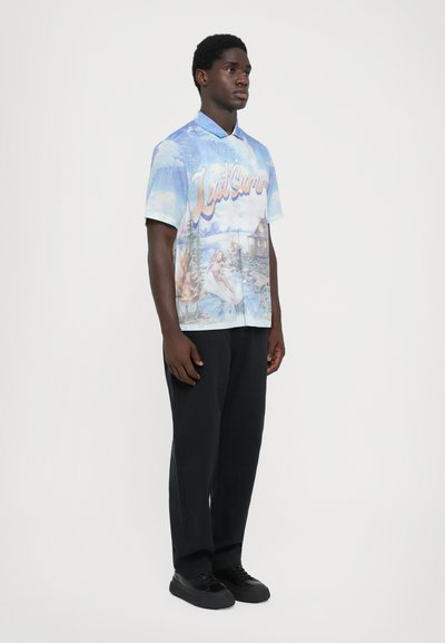 Short-sleeve, collared shirt features a blue and pastel graphic design with scenes and text, paired with black trousers and shoes.