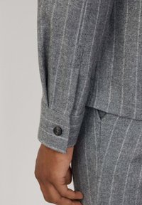 Blazer grigio in lana con un sottile motivo a righe. Presenta un polsino con bottoni e un design strutturato, che mette in evidenza una silhouette sartoriale.