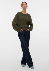 Oliwkowy sweter dzianinowy o prążkowanej fakturze i okrągłym dekolcie, zestawiony z ciemnoniebieskimi spodniami typu wide-leg oraz jasnoniebieskimi butami na szpic.
