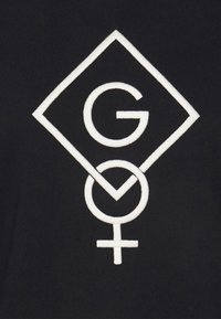 Černá látka s vyšívaným bílým logem, ve tvaru diamantu, se začleněným písmenem "G" a ženským symbolem v designu.