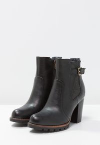 Bottines noires en cuir avec une finition lisse. Dotées d'une fermeture éclair sur le côté, d'un accent à boucle et d'un talon épais. Semelle texturée.