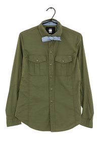 Camicia verde oliva a maniche lunghe con colletto a bottoni, due tasche sul petto e un'accento di papillon azzurro chiaro. Tessuto dalla consistenza liscia.