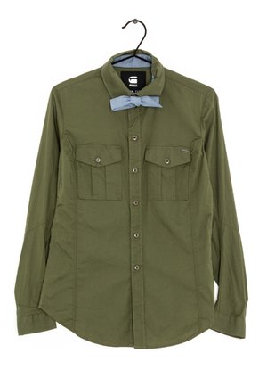 Camicia verde oliva a maniche lunghe con colletto a bottoni, due tasche sul petto e un'accento di papillon azzurro chiaro. Tessuto dalla consistenza liscia.
