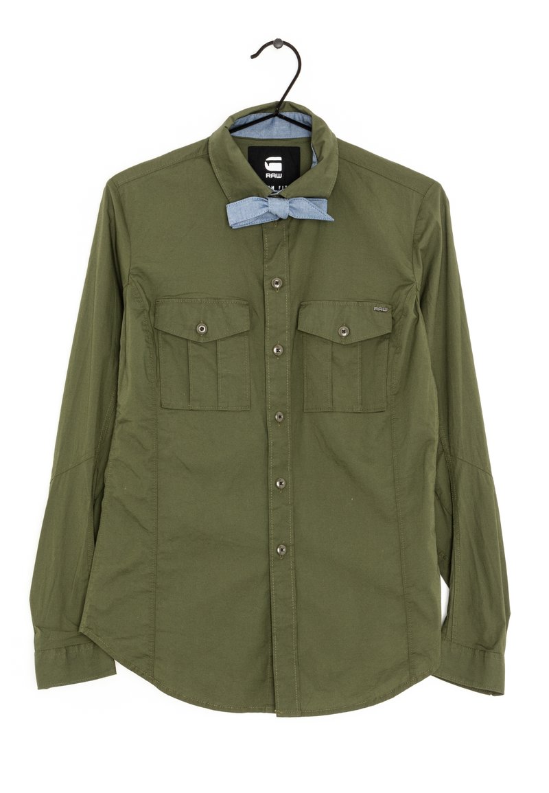 Olivgrön långärmad skjorta med knäppbar krage, två bröstfickor och en ljusblå fluga som accent. Slät tygtextur.