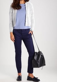 Cardigan blanc texturé, haut bleu, pantalon bleu marine, sac seau noir et chaussures slip-on bleu marine. Silhouette moderne et ajustée avec un design en couches.