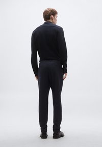 Námornícka modrá polokošeľa s dlhým rukávom a golierom, skombinovaná s tmavými nohavicami. Tkanina pôsobí hladko, s minimálnymi detailmi a čistou siluetou.