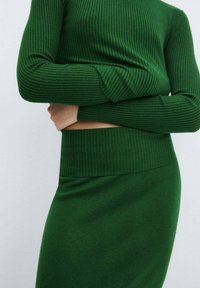 Ensemble en tricot côtelé vert comprenant un pull et une jupe. Le pull présente des manches longues et une coupe ajustée ; la jupe a une taille élastique et une texture lisse.