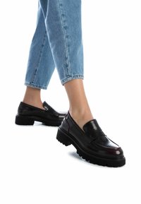 Mocassini neri in pelle con finitura lucida, suola in gomma spessa e dettagli di cucitura discreti, abbinati a jeans cropped azzurri chiari.