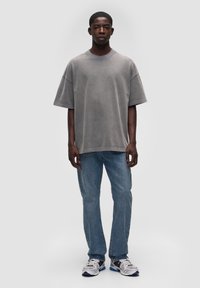 Przesadnie duża szara koszulka bawełniana z krótkim rękawem, w połączeniu z jasnoniebieskimi dżinsami i szarymi trampkami z czarnymi i niebieskimi akcentami.