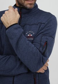 Fleece-Jacke mit Reißverschluss in Marineblau. Mit hohem Kragen, schwarzen Akzenten und einem Logo auf der Brust. Inklusive Reißverschlusstaschen und strukturiertem Stoff.