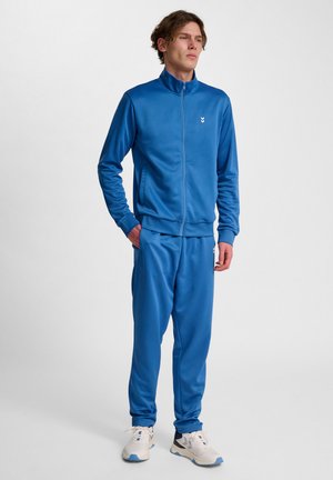 Blauwe trainingspak gemaakt van glad, lichtgewicht materiaal. Beschikt over een ritsjack met hoge kraag en bijpassende broek met elastische tailleband.
