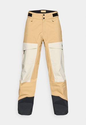 Beige and white outdoor pants with black accents. Features cargo pockets, dual button closure, and a durable texture suitable for various conditions.