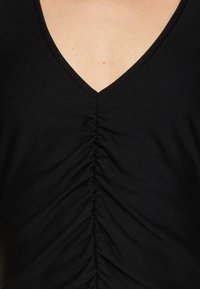 Czarny top z materiału, z głębokim dekoltem w kształcie litery V i marszczoną teksturą wzdłuż środka, tworzącą pionowe linie. Miękki, elastyczny materiał.