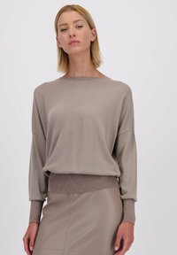 Lichtbeige gebreide trui met lange mouwen en een ronde halslijn, met een glansaccent aan de mouwen en de tailleband. Gladde textuur.